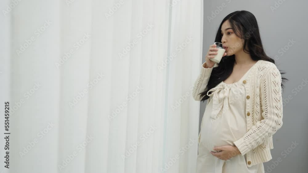 pregnant woman drinking a milk at the window in bedroom pregnant woman drinking a milk at the window in bedroom