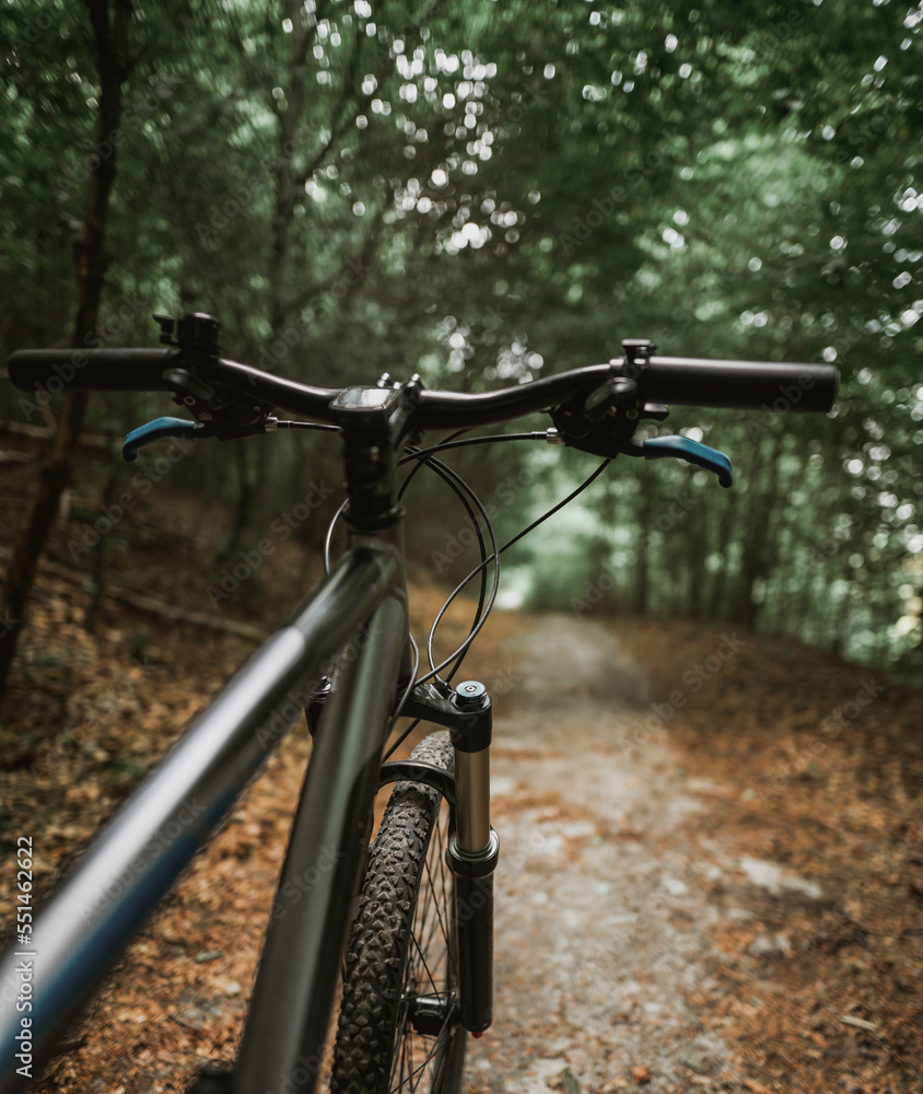 Mountain bike handlebar viewed from the first-person perspective.handlebar and the forest trail. Concept of spending time outdoors while bikeriding Mountain bike handlebar viewed from the first-person perspective.handlebar and the forest trail. Concept of spending time outdoors while bikeriding