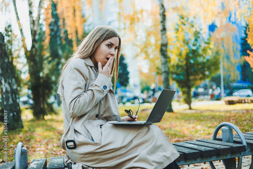 A cute fair-haired young woman is sitting in an autumn park on a bench and working on a laptop. Remote work A cute fair-haired young woman is sitting in an autumn park on a bench and working on a laptop. Remote work
