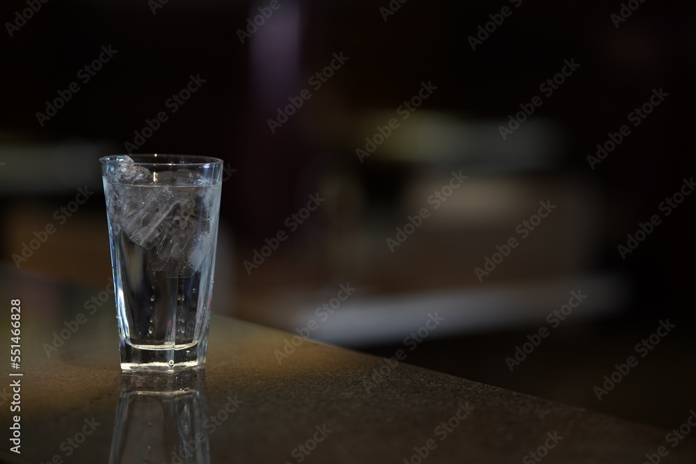 A glass of water with ice on a dark environment, low key light photography
