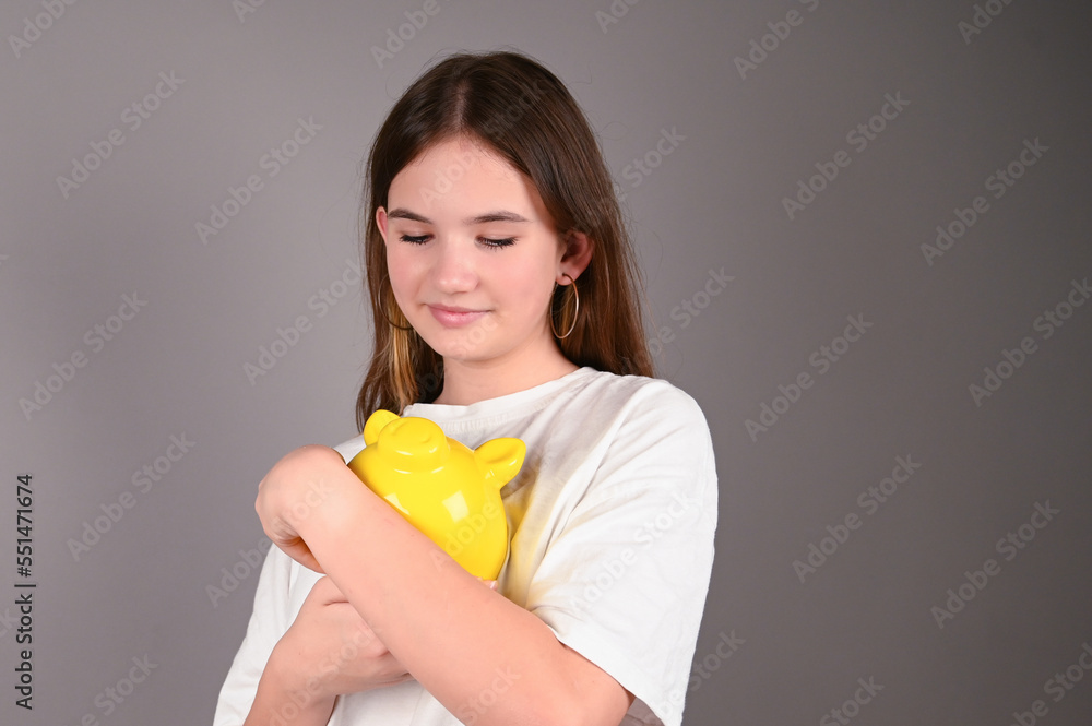 Teenage girl holding yellow piggy bank. Young girl with yellow piggy bank on gray. Save money and financial investment Teenage girl holding yellow piggy bank. Young girl with yellow piggy bank on gray. Save money and financial investment