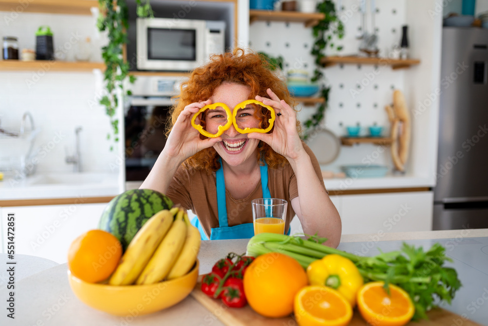 Photo of young woman smiling and holding pepper circles on her eyes while cooking salad with fresh vegetables in kitchen interior at home Photo of young woman smiling and holding pepper circles on her eyes while cooking salad with fresh vegetables in kitchen interior at home