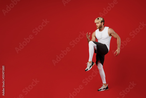 Full body side profile view young strong sporty toned sportsman man wearing white clothes spend time in home gym prepare to run start isolated on plain red background. Workout sport fit body concept.