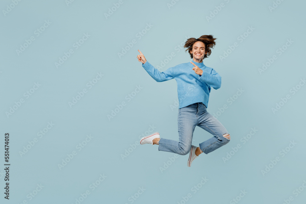 Full body young woman in knitted sweater look camera jump high point index fingers aside on workspace area mock up isolated on plain pastel light blue cyan background studio People lifestyle concept