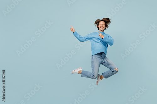 Full body young woman in knitted sweater look camera jump high point index fingers aside on workspace area mock up isolated on plain pastel light blue cyan background studio People lifestyle concept photo