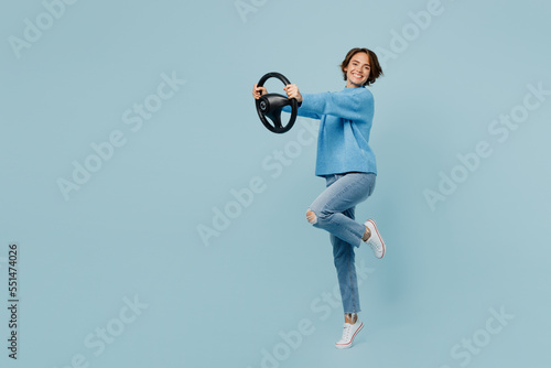 Full body young smiling cheerful fun woman in knitted sweater look camera hold steering wheel driving car isolated on plain pastel light blue cyan background studio portrait People lifestyle concept photo