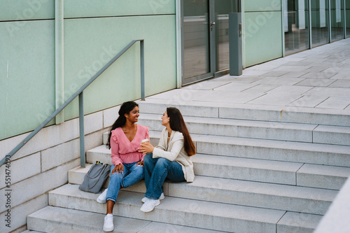 Young indian women smiling and drinking coffee while sitting on stairs