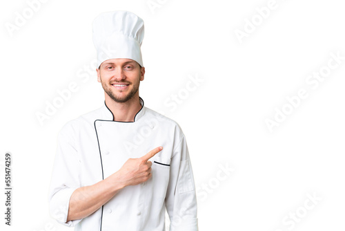 Young caucasian chef over isolated chroma key background pointing to the side to present a product photo