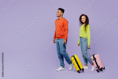 Full body young couple two friends man woman in casual clothes together hold suitcase bag isolated on plain purple background. Tourist travel abroad in free time rest. Air flight trip journey concept.