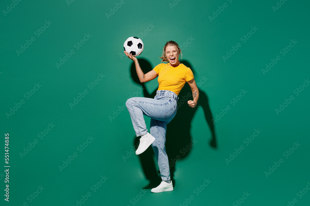 Full body side view excited young woman fan in yellow t-shirt cheer up support football sport team hold soccer ball watch tv live stream do winner gesture celebrate isolated on dark green background
