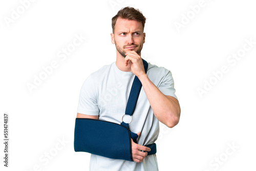 Young caucasian man with broken arm and wearing a sling over isolated chroma key background having doubts and thinking