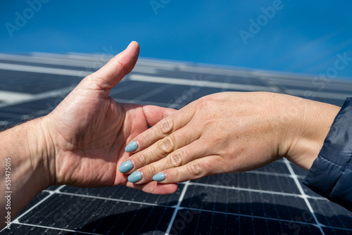 two pairs of hands shaking hands after making a deal on the background of solar panels.