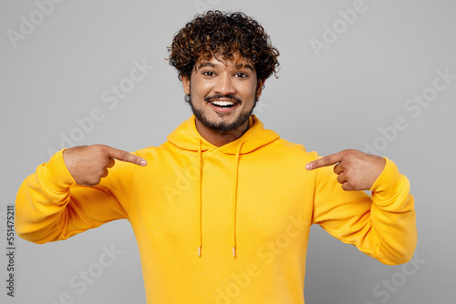 Young cheerful Indian man 20s he wear casual yellow hoody point index fingers on himself or hoodie with blank print design isolated on plain grey background studio portrait. People lifestyle portrait.