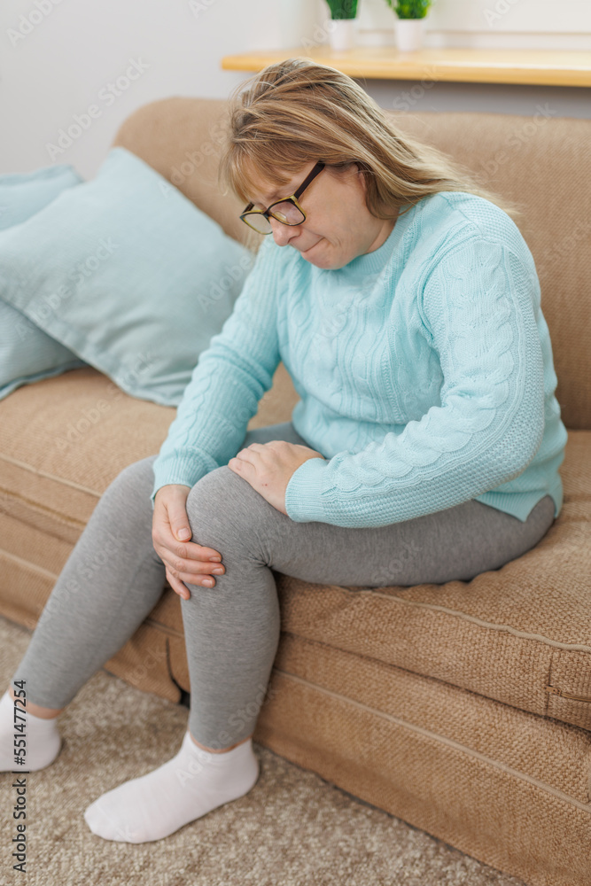 Mature woman suffering from knee ache on sofa Mature woman suffering from knee ache on sofa