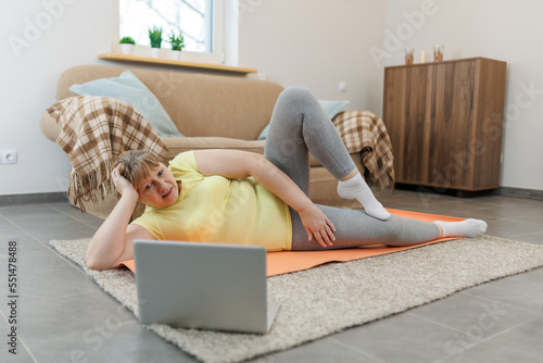 Mature woman exercising on the floor in front of laptop in the living room at home