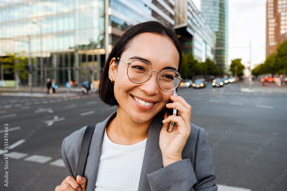Young woman smiling and talking on cellphone while standing at the city street Young woman smiling and talking on cellphone while standing at the city street