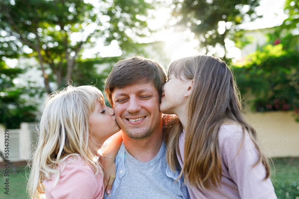 Smiling father with daughters kissing him on cheek at park Smiling father with daughters kissing him on cheek at park