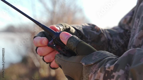 a military man in a camouflage uniform and tactical gloves adjusts a walkie-talkie to communicate with units Secure communication of the Ukrainian army during the war. encryption of radio broadcasts