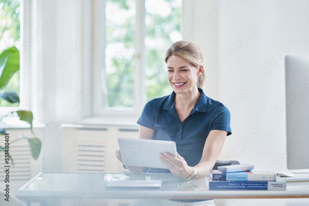 Happy female doctor using tablet PC at desk in medical practice Happy female doctor using tablet PC at desk in medical practice