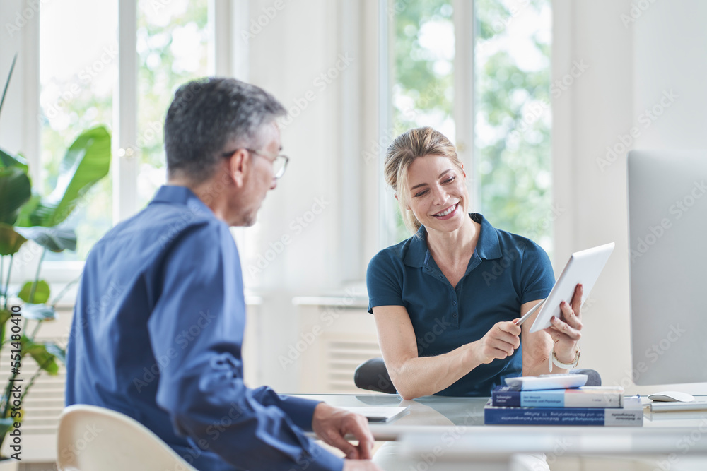 Smiling female doctor discussing over tablet PC with patient in medical practice Smiling female doctor discussing over tablet PC with patient in medical practice