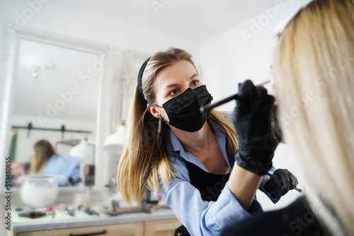 Blond beautician applying make-up on customer's face in salon photo