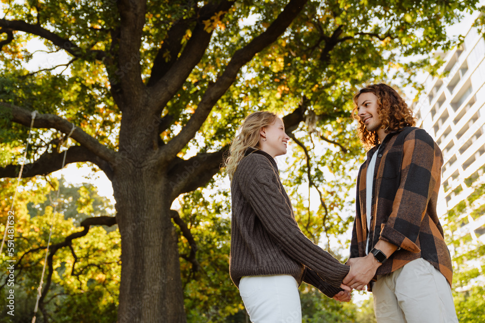 Young loving couple smiling and looking at each other while standing outdoors in park