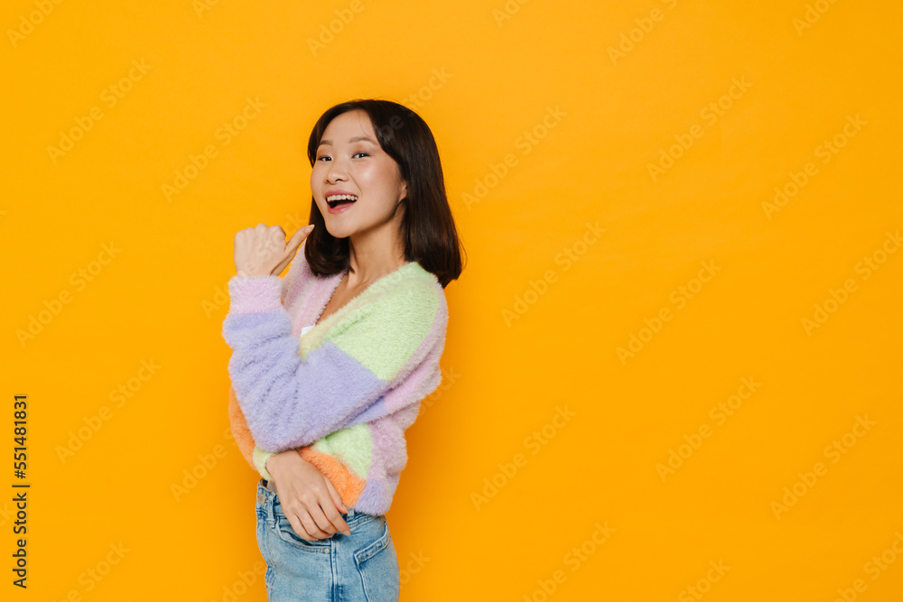 Young asian girl pointing away with thumb isolated over yellow background Young asian girl pointing away with thumb isolated over yellow background