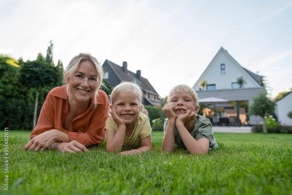 Smiling woman with children leaning on elbows in back yard Smiling woman with children leaning on elbows in back yard