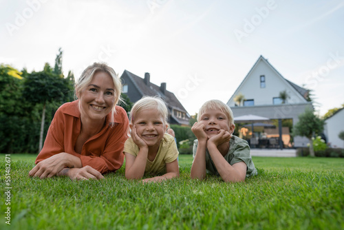 Smiling woman with children leaning on elbows in back yard photo