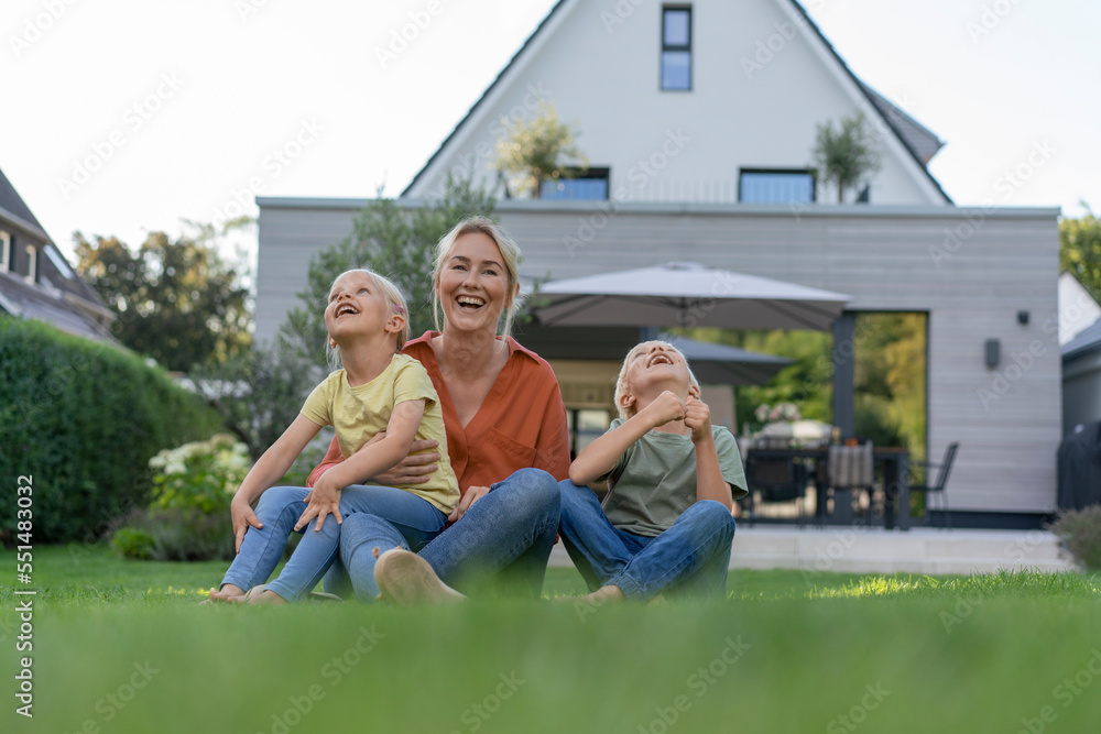 Happy mother with son and daughter sitting on grass in back yard