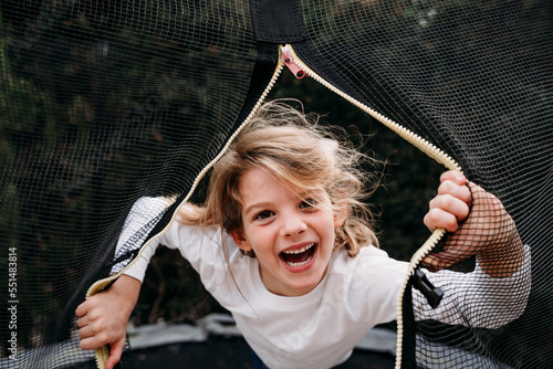 Happy girl looking through net on trampoline in garden photo