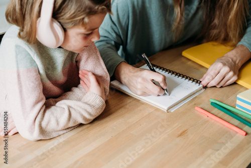 Hand of woman writing on notebook by girl at home photo