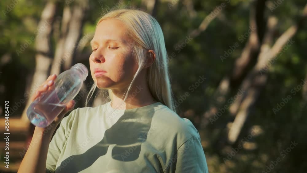 A pretty young blonde tourist woman drinks water from a bottle in a beautiful forest at sunset. Quenching thirst in the wild. Pure natural water. High quality 4k footage A pretty young blonde tourist woman drinks water from a bottle in a beautiful forest at sunset. Quenching thirst in the wild. Pure natural water. High quality 4k footage