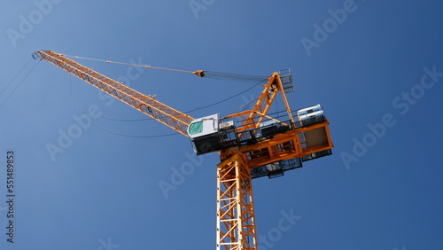 Yellow tower crane luffing boom soars isolated into blue sky