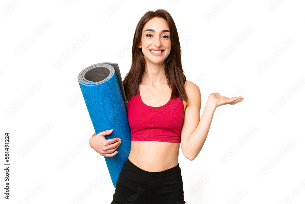 Young sport caucasian woman going to yoga classes while holding a mat over isolated chroma key background extending hands to the side for inviting to come Young sport caucasian woman going to yoga classes while holding a mat over isolated chroma key background extending hands to the side for inviting to come
