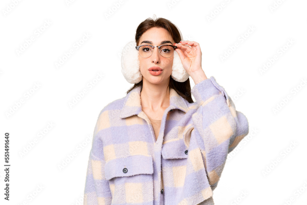 Young caucasian woman wearing winter muffs over isolated chroma key background with glasses and surprised Young caucasian woman wearing winter muffs over isolated chroma key background with glasses and surprised