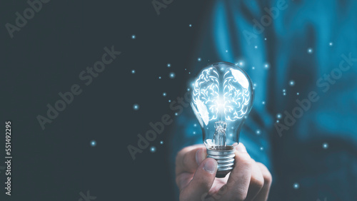 Obraz na płótnie Businessman hand holding lightbulb with glowing virtual brain and  connection line to creative smart thinking for inspiration and innovation with network concept