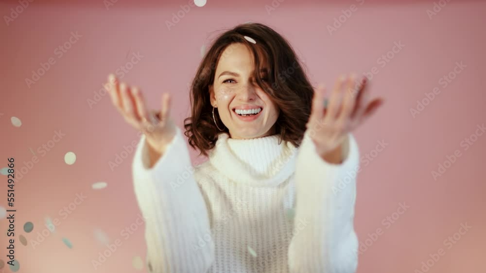 Beautiful young adult woman in cosy white sweater. Brunette female with confetti on pink background. 2023 celebration holiday light consept. Beautiful young adult woman in cosy white sweater. Brunette female with confetti on pink background. 2023 celebration holiday light consept.