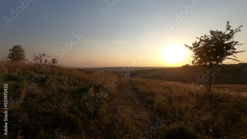 Wallpaper Mural Cinematic FPV drone view of loving young man and woman hugging, kissing and holding hands on hilly meadow with green grass in bright sunlight, during beautiful summer sunset in nature, slow motion. Torontodigital.ca