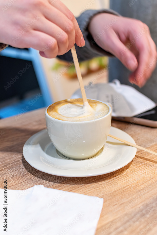 A woman holding coffee spoon and stirring hot coffee on wooden table. A woman holding coffee spoon and stirring hot coffee on wooden table.