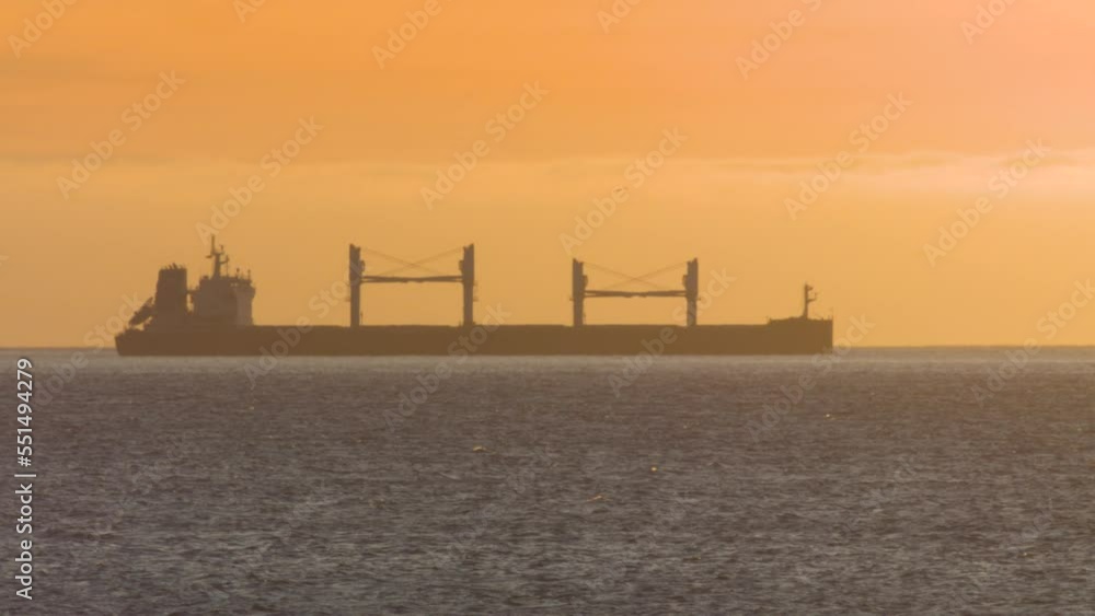Cargo ship on sunset silhouette. Bulker in the waves. Big sun behind the vessel. Dark vessel in the Atlantic ocean. Side view. Golden hour. Cargo ship on sunset silhouette. Bulker in the waves. Big sun behind the vessel. Dark vessel in the Atlantic ocean. Side view. Golden hour.