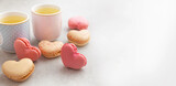 French macaroons in the shape of a heart, two tea cups with chamomile tea on a gray background with copy space. Concept - holiday, Mother's day, Valentine's day, gift