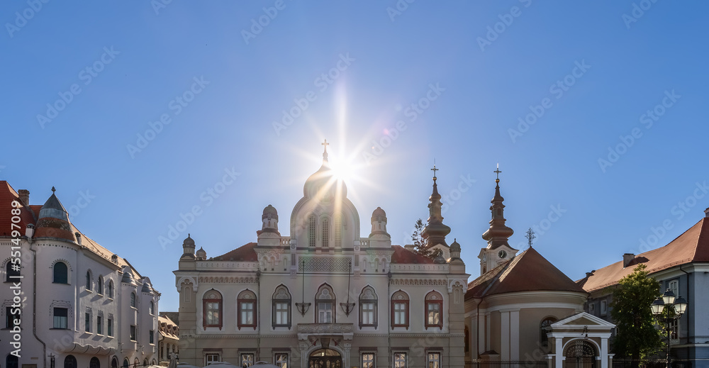 Obraz premium Setting sun rays shine brightly above facade roof of diocese (eparchy) of Serbian Orthodox Church (Episcopia Ortodoxa Sarba) on central Union Square (Piata Unirii) in Timisoara, Romania