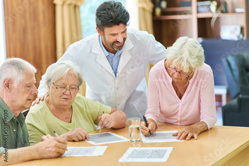 Doctor takes care of seniors group solving puzzles © Robert Kneschke