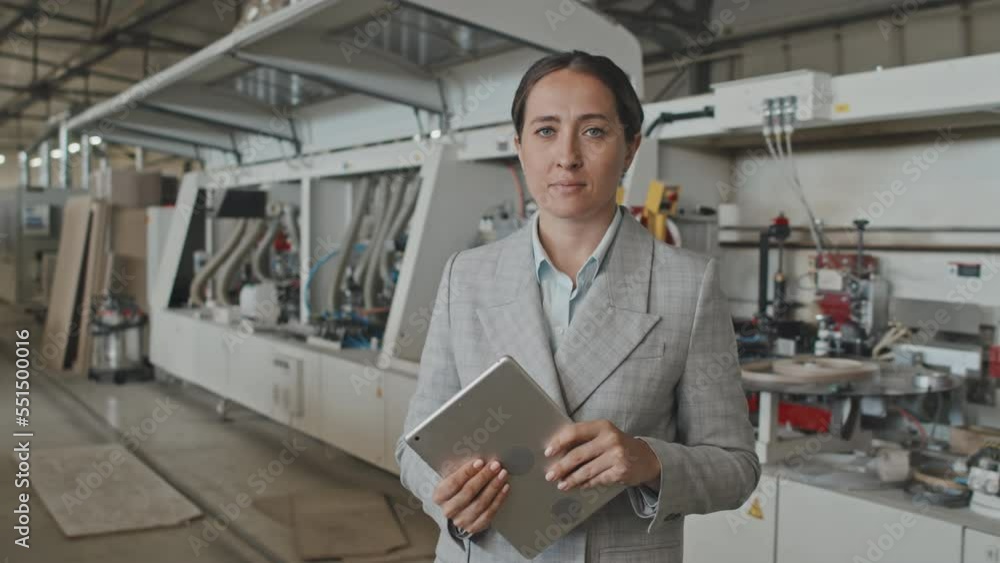 Medium waist up shot of female manager in formalwear holding digital tablet and posing for camera at work in furniture factory. Suitable for deepfake generation or face swap Medium waist up shot of female manager in formalwear holding digital tablet and posing for camera at work in furniture factory. Suitable for deepfake generation or face swap