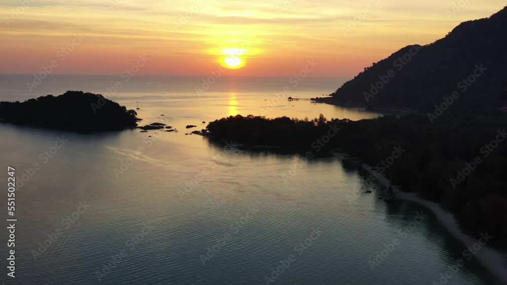 Tranquil sunset landscape aerial shot capturing pulau burau islet and beautiful orange glowing sun setting below the horizon at pantai kok beach, island shore bounded by strait of malacca, Langkawi. Tranquil sunset landscape aerial shot capturing pulau burau islet and beautiful orange glowing sun setting below the horizon at pantai kok beach, island shore bounded by strait of malacca, Langkawi.