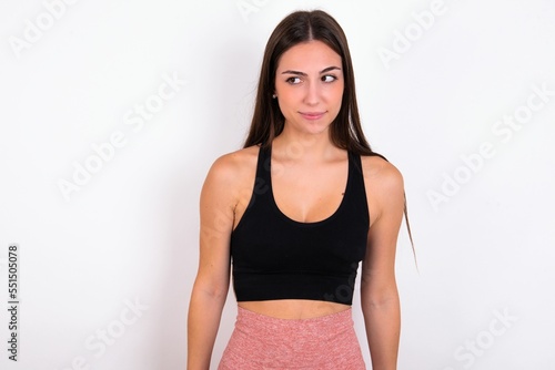 Amazed puzzled Young caucasian woman wearing sportswear over white background , curves lips and has worried look, sees something awful in front.