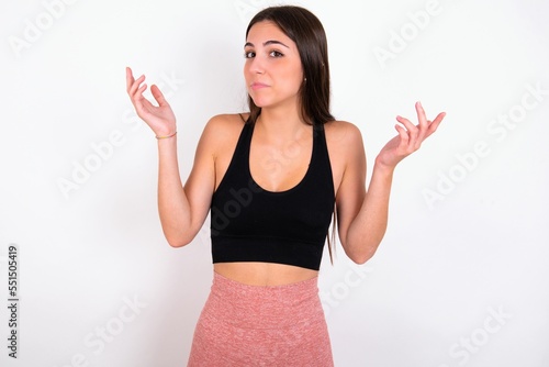 Puzzled and clueless Young caucasian woman wearing sportswear over white background  with arms out, shrugging shoulders, saying: who cares, so what, I don't know. © Jihan