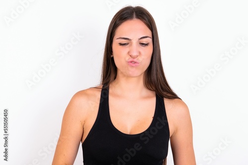Young caucasian woman wearing sportswear over white background crosses eyes, puts lips, makes grimace with awkward expression has fun alone, plays fool.