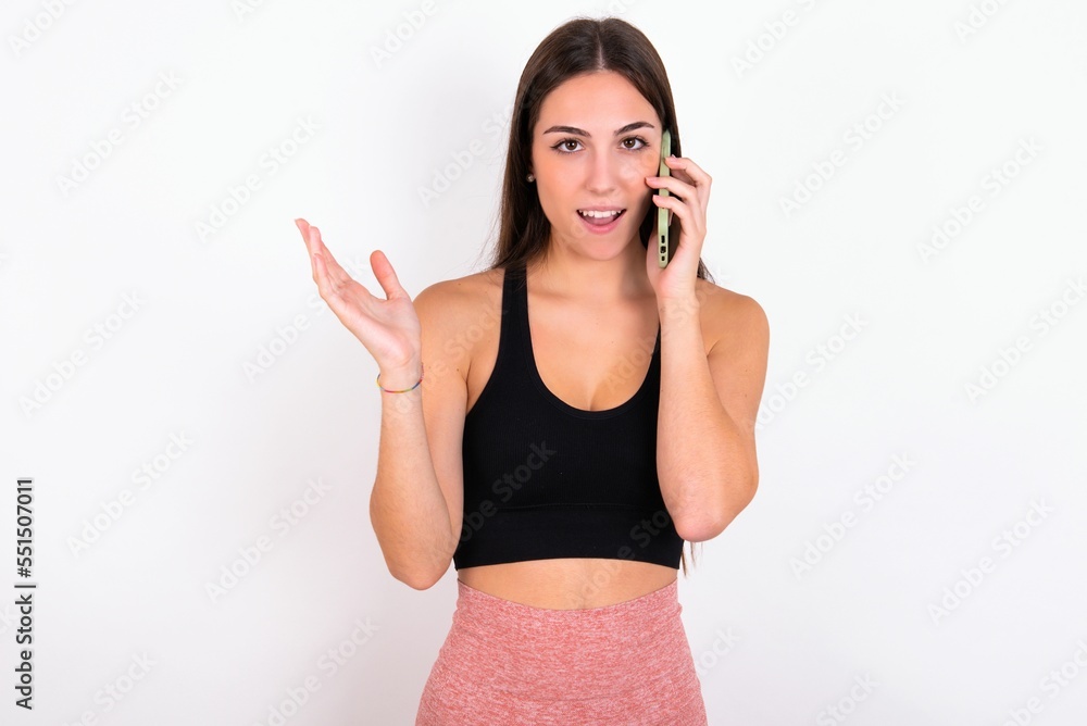 Young caucasian woman wearing sportswear over white background talking on the phone stressed with hand on face, shocked with shame and surprise face, angry and frustrated. Fear and upset for mistake. Young caucasian woman wearing sportswear over white background talking on the phone stressed with hand on face, shocked with shame and surprise face, angry and frustrated. Fear and upset for mistake.